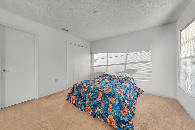 bedroom with a textured ceiling, light colored carpet, and a closet