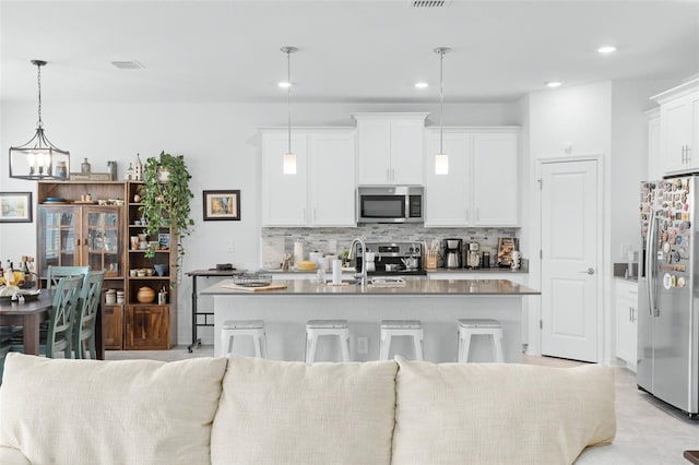 kitchen featuring a kitchen island with sink, tasteful backsplash, decorative light fixtures, white cabinetry, and stainless steel appliances