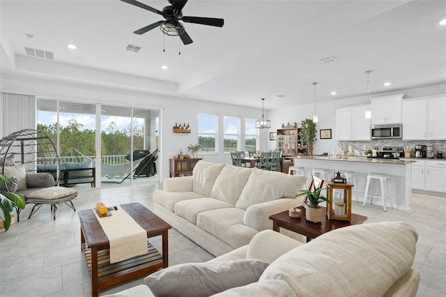 tiled living room with ceiling fan and a raised ceiling