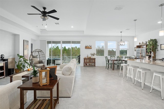 living room featuring ceiling fan with notable chandelier and a tray ceiling