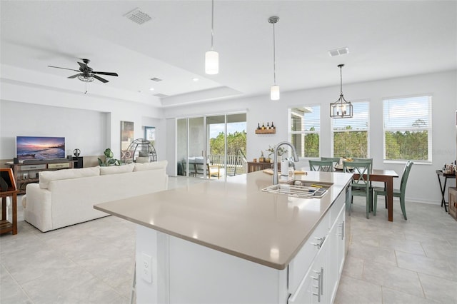 kitchen with a sink, white cabinets, a tray ceiling, and visible vents