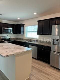 kitchen with appliances with stainless steel finishes, light hardwood / wood-style flooring, a kitchen island, and sink