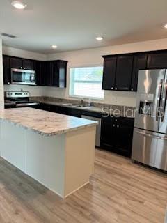 kitchen with light stone countertops, sink, a center island, stainless steel appliances, and light wood-type flooring