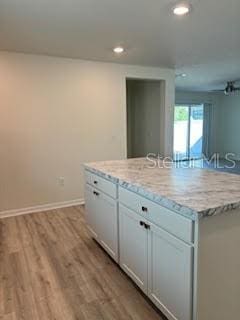 kitchen with white cabinets, a center island, light stone countertops, and light hardwood / wood-style flooring