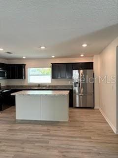 kitchen with stainless steel refrigerator with ice dispenser, a center island, light hardwood / wood-style flooring, and electric range