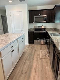 kitchen with white cabinets, stainless steel appliances, light stone countertops, and sink