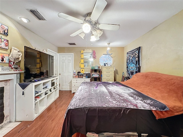 bedroom featuring wood-type flooring, ceiling fan, and a tiled fireplace