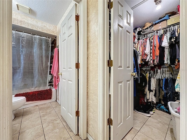 bathroom with tile patterned floors, toilet, shower / bath combo with shower curtain, and a textured ceiling