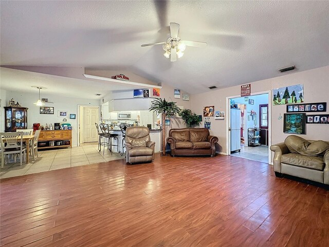 living room with ceiling fan, light hardwood / wood-style floors, a textured ceiling, and vaulted ceiling