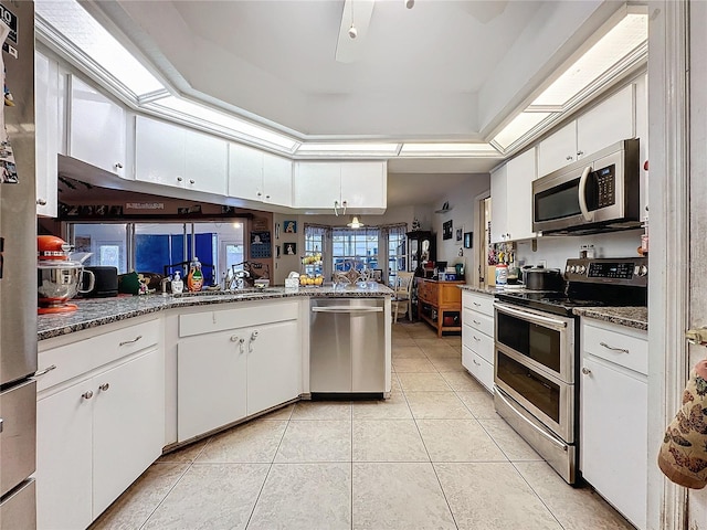 kitchen featuring stainless steel appliances, light tile patterned floors, kitchen peninsula, dark stone counters, and white cabinets