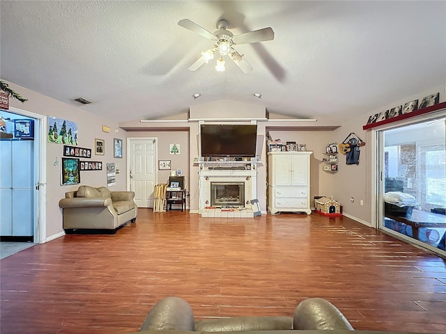 living room featuring a textured ceiling, ceiling fan, a tile fireplace, wood-type flooring, and lofted ceiling