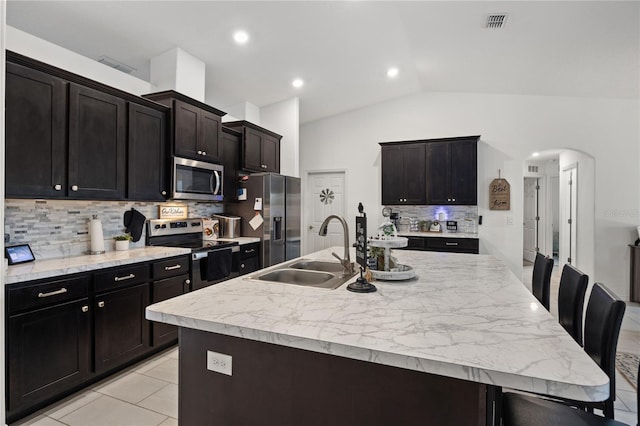 kitchen featuring tasteful backsplash, stainless steel appliances, a kitchen island with sink, sink, and lofted ceiling