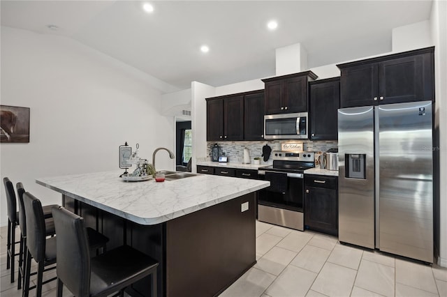 kitchen featuring sink, stainless steel appliances, backsplash, a kitchen island with sink, and light tile patterned flooring