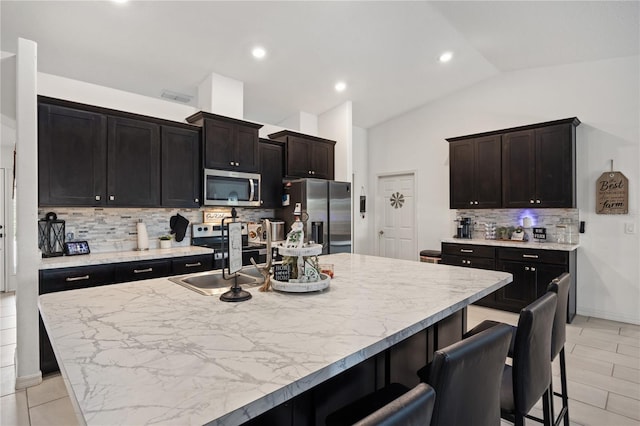 kitchen featuring sink, lofted ceiling, a kitchen bar, a kitchen island with sink, and appliances with stainless steel finishes