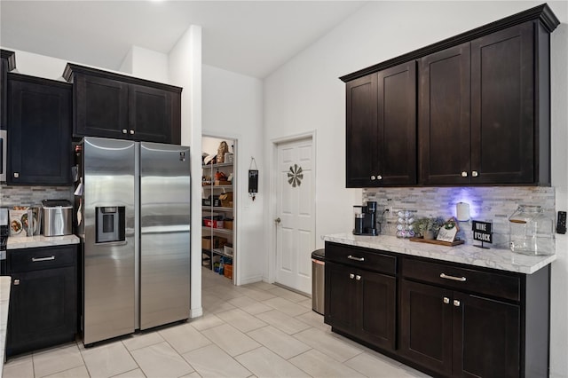 kitchen featuring tasteful backsplash, dark brown cabinetry, stainless steel fridge with ice dispenser, and light stone counters