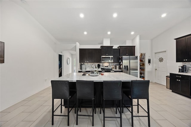 kitchen with backsplash, a breakfast bar, an island with sink, and stainless steel appliances