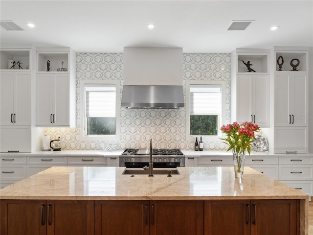 kitchen with a center island with sink, white cabinetry, and wall chimney range hood