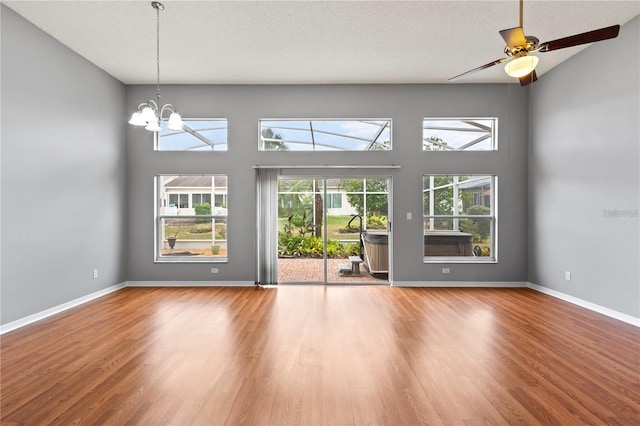 unfurnished living room with ceiling fan with notable chandelier, a textured ceiling, and hardwood / wood-style flooring