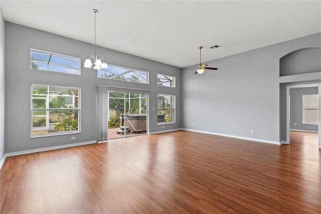 unfurnished living room featuring hardwood / wood-style floors, ceiling fan with notable chandelier, and a high ceiling