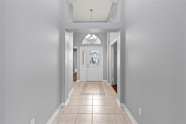 doorway to outside with a chandelier, a towering ceiling, and light tile patterned flooring