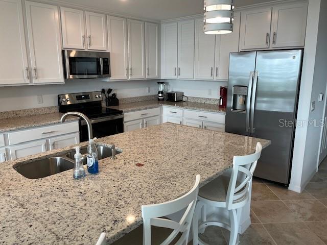 kitchen with appliances with stainless steel finishes, light stone counters, white cabinetry, and sink