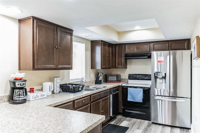 kitchen with dark brown cabinetry, sink, a tray ceiling, black appliances, and light wood-type flooring