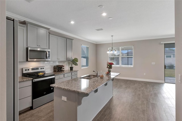 kitchen featuring light stone counters, gray cabinetry, stainless steel appliances, a kitchen island with sink, and sink