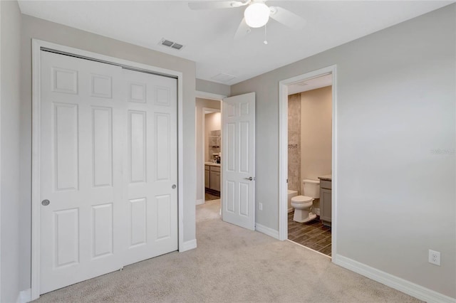 unfurnished bedroom featuring light carpet, ensuite bathroom, a closet, and ceiling fan