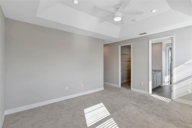 unfurnished bedroom featuring ensuite bath, a raised ceiling, a spacious closet, and a closet