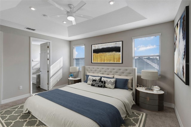 carpeted bedroom with a raised ceiling, ensuite bath, and ceiling fan