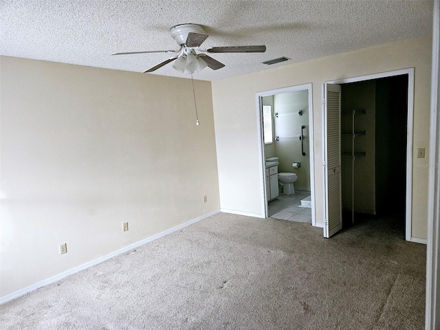 unfurnished bedroom featuring a closet, ensuite bathroom, ceiling fan, and light colored carpet