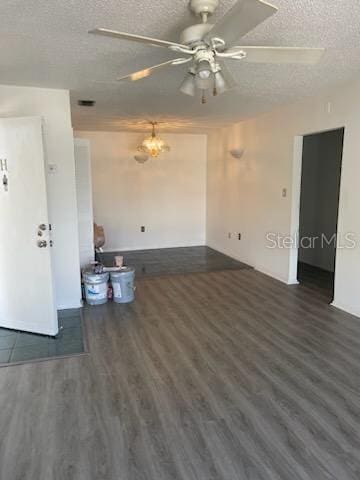 unfurnished living room featuring ceiling fan with notable chandelier, dark hardwood / wood-style flooring, and a textured ceiling