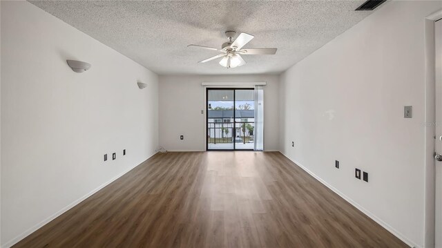 empty room with a textured ceiling, wood finished floors, a ceiling fan, and baseboards