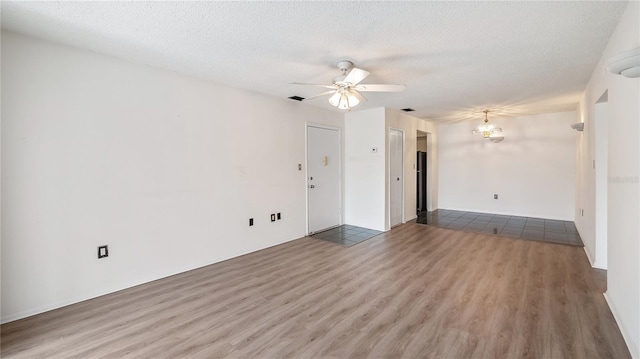 spare room with ceiling fan with notable chandelier, visible vents, a textured ceiling, and wood finished floors