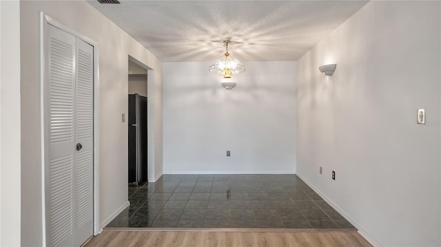 unfurnished dining area featuring a textured ceiling, a notable chandelier, wood finished floors, and baseboards