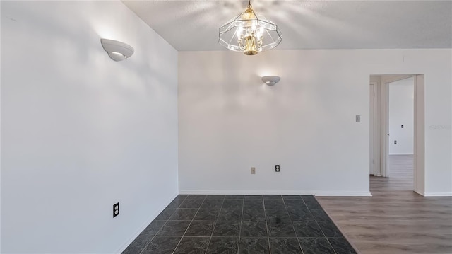 empty room featuring baseboards, wood finished floors, and a notable chandelier