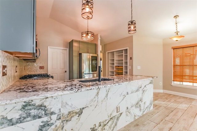 kitchen featuring pendant lighting, sink, vaulted ceiling, stainless steel fridge, and light stone countertops