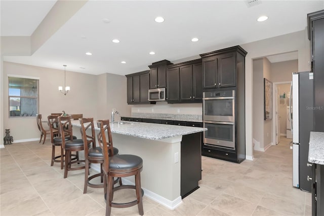 kitchen featuring light stone countertops, sink, stainless steel appliances, decorative light fixtures, and a kitchen island with sink