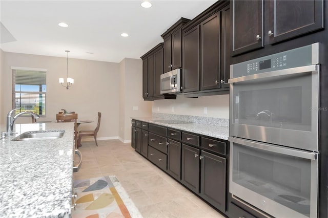 kitchen with sink, light stone counters, a notable chandelier, dark brown cabinets, and appliances with stainless steel finishes