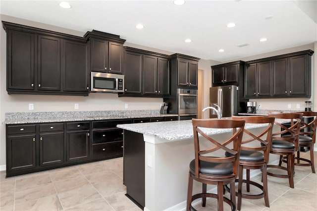 kitchen featuring a breakfast bar area, a kitchen island with sink, light stone countertops, and stainless steel appliances