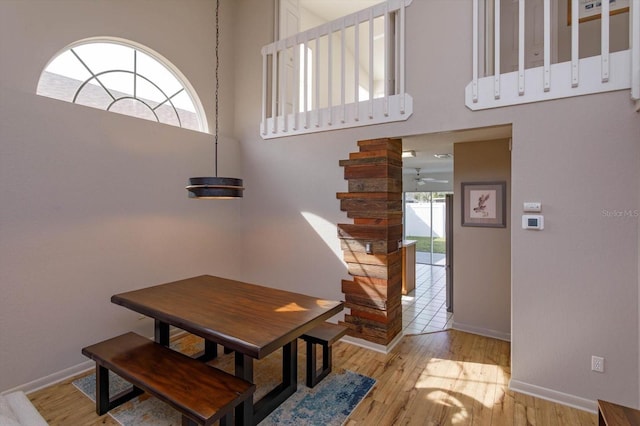 dining area with ceiling fan, a towering ceiling, and light wood-type flooring