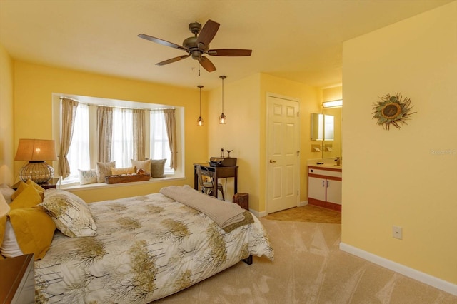 bedroom with ceiling fan, light colored carpet, and ensuite bath