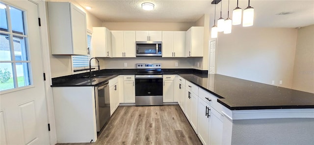 kitchen featuring white cabinets, decorative light fixtures, stainless steel appliances, and a textured ceiling