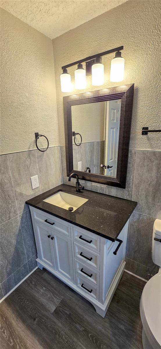 bathroom featuring a textured ceiling, vanity, hardwood / wood-style flooring, and tile walls