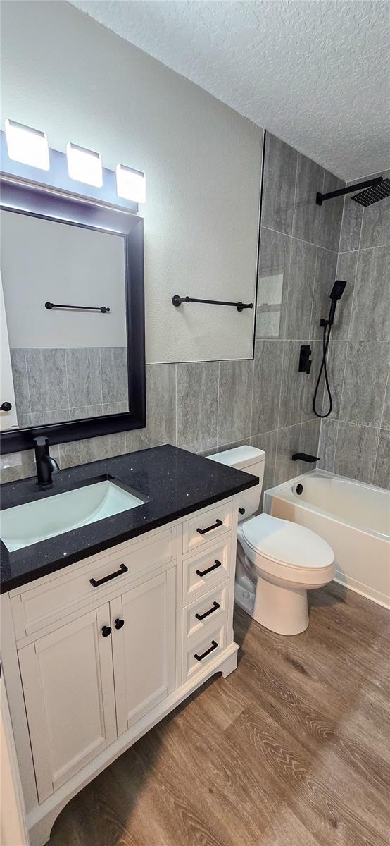 full bathroom featuring vanity, hardwood / wood-style flooring, toilet, a textured ceiling, and tile walls