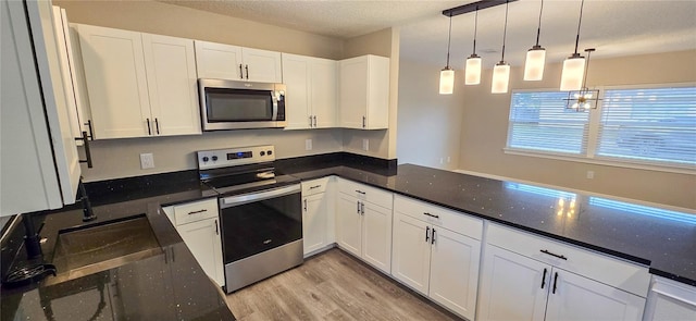 kitchen featuring sink, dark stone countertops, appliances with stainless steel finishes, decorative light fixtures, and white cabinetry