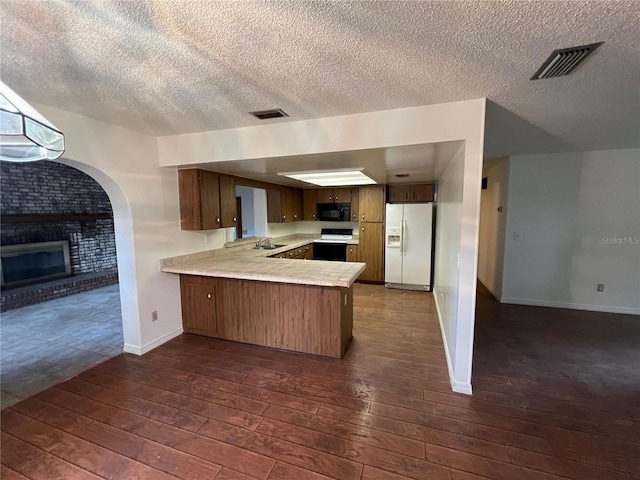 kitchen with sink, white appliances, kitchen peninsula, and a brick fireplace