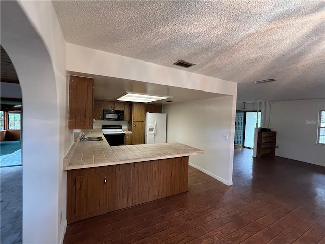 kitchen with sink, dark hardwood / wood-style floors, kitchen peninsula, tile countertops, and white appliances