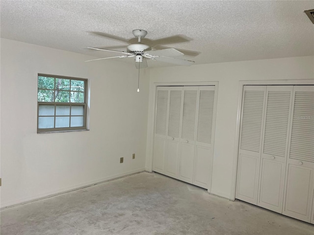 unfurnished bedroom with a textured ceiling, two closets, and ceiling fan