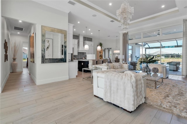 living room with ceiling fan with notable chandelier, a tray ceiling, and ornamental molding